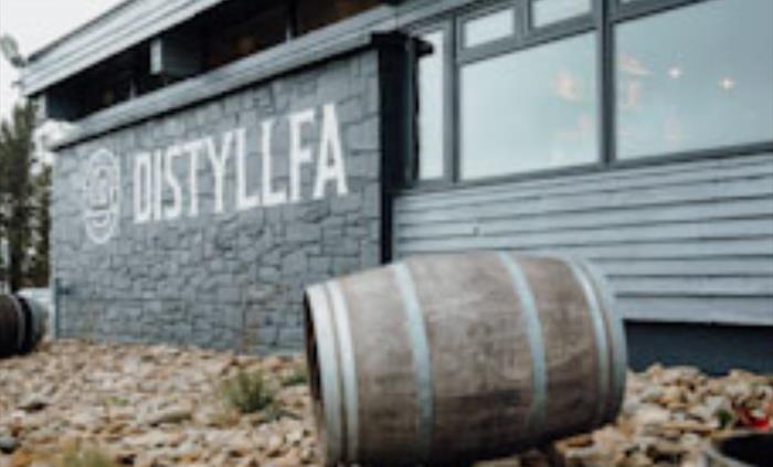 Distillery exterior with barrel in foreground and logo on the wall in the background